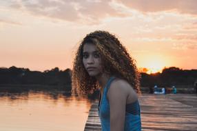 Portrait of the beautiful girl with curly hair, on the pier, at colorful and beautiful sunset