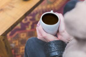 Woman holding cup of brewed coffee in hands, above the colorful floor