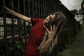 Girl with blonde and dark hair, in glasses and red t-shirt, posing near the fence, outdoors