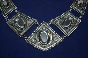 Close-up of the shiny jewellery necklace with patterns, at blue background