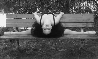 Black and white photo of the ballerina, posing on the wooden bench, near the plants