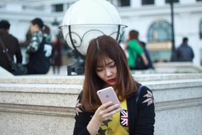 young asian woman with iphone on city street in blurred background