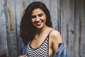 Portrait of the smiling girl in bra and denim jacket, near the wooden wall