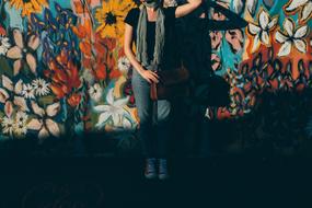 Woman with scarf, posing neat the wall with colorful graffities in sunlight and shadow