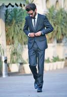 Man in glasses and suit with tie, walking on the path, near the plants