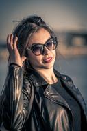 Woman in black jacket, with shiny sunglasses, posing outdoors