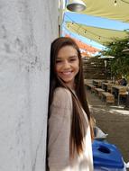 Portrait of the beautiful, smiling girl near the wall and tables with other person