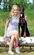 happy young Blonde Woman sits with Doberman Dog