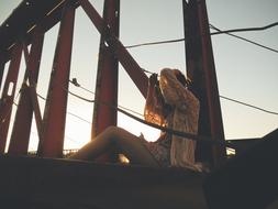 Girl sits on metal construction at evening