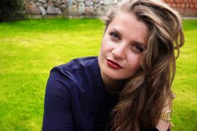 Portrait of the posing woman with make-up, on the green grass, near the wall