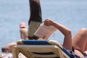 reading a book while lying on a lounger on the beach