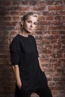 Blonde woman in black clothing, posing near the brick wall