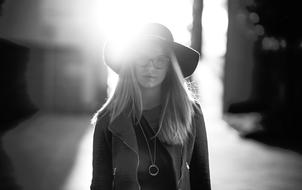 Black and white portrait of the woman with glasses, in hat, in light