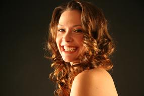 Portrait of the smiling woman with curly hair and bare shoulders at black background