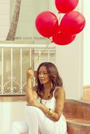 Woman, sitting with the flying, red balloons in the hand, on the stairs