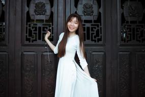 asian girl in a white dress stands on the background of doors
