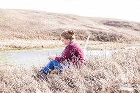photo of a girl sitting on dry grass on a hill