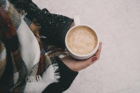 cup of foamy coffee in female hands in the cold