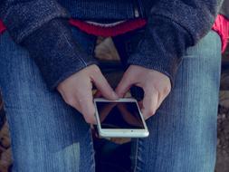 a guy holding a smartphone in his hands while sitting on a bench