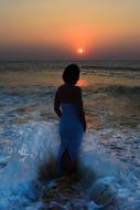 Back view of the woman, in the dress, in the beautiful sea, with the waves, at colorful and beautiful sunset