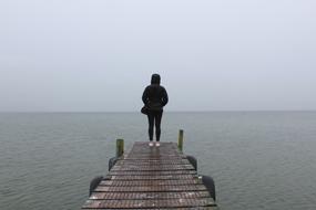 lonely girl in a black jacket on a pier on the lake