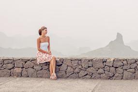 Young caucasian Woman sits on stone fence at scenic mountains, spain, canary islands