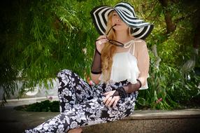 Portrait of a blonde woman in black and white, striped hat, near the green plants