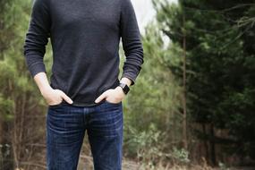 Man, holding hands in jeans, among the green trees, in the beautiful forest