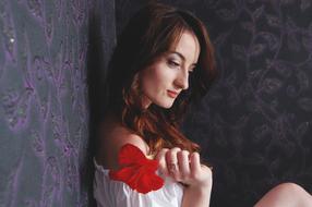 Profile portrait of the smiling woman, with the make-up, and beautiful, red flower, near the patterned walls