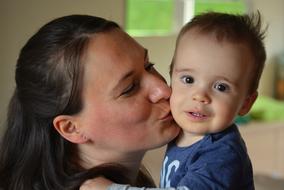 Smiling mother, kissing the cute child, at blurred background