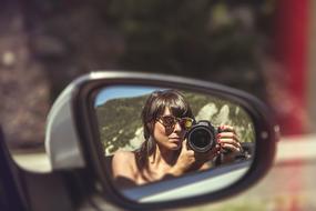 woman with a camera is reflected in the side mirror of an auto
