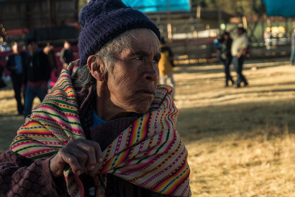 Portrait of the Peruvian woman, in light and shadows, covered in the clothing, near the other people, in