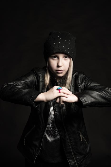 Blonde girl in black and white clothing and hat, and with the colorful ring, at black background