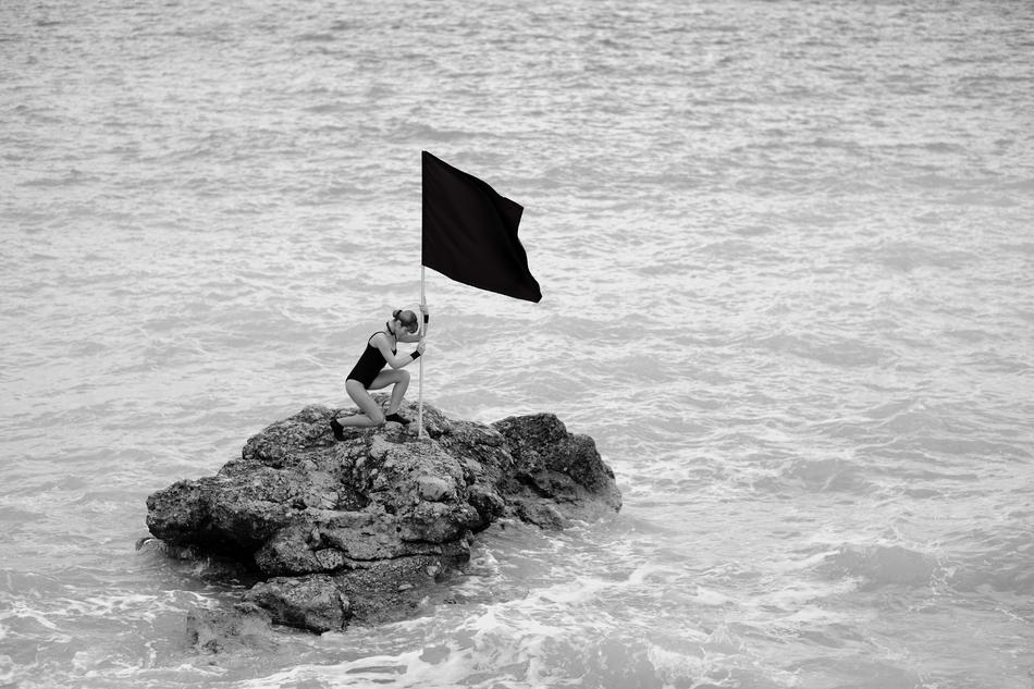 woman and flag on a stone in the ocean