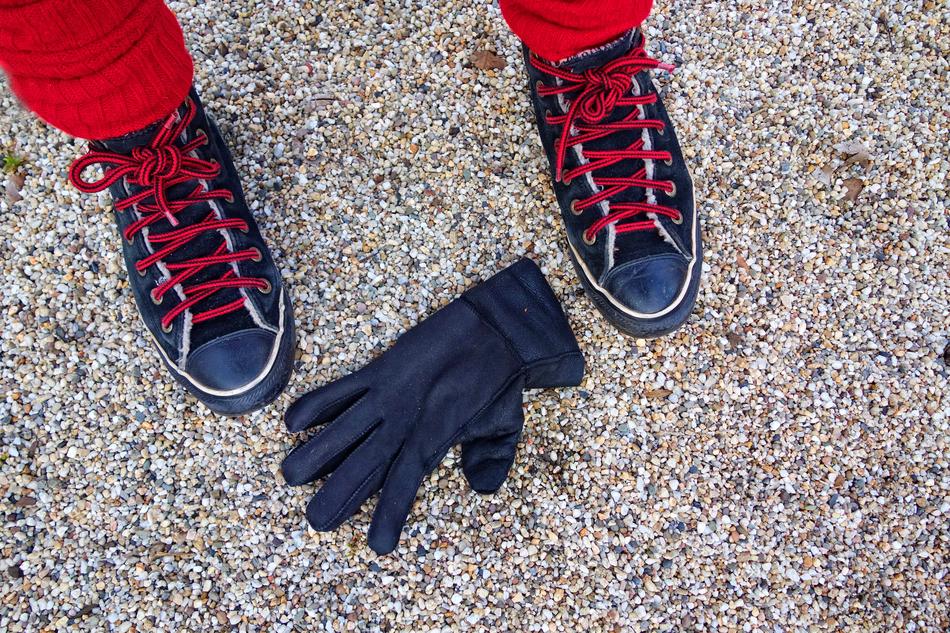 Close-up of the dark glove near the person in sneakers, on the ground