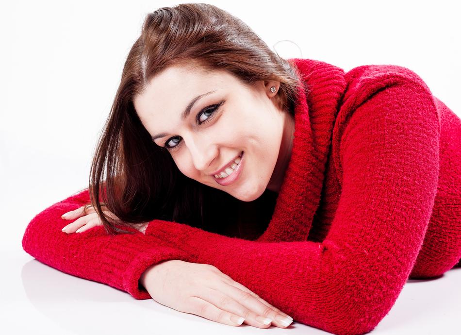 Smiling woman in red jumper, laying on white surface
