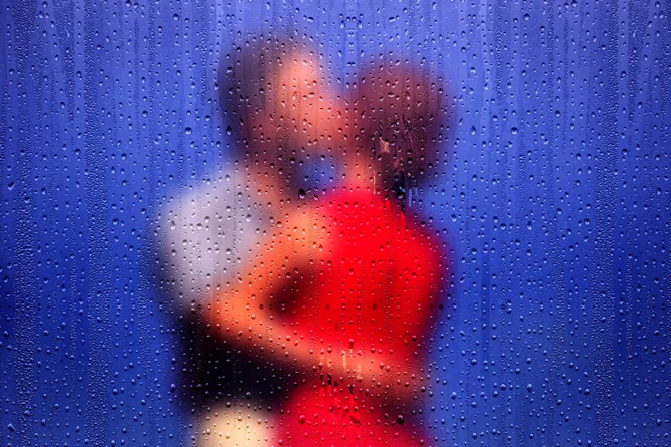 View of the pair kissing behind the blue window with water drops