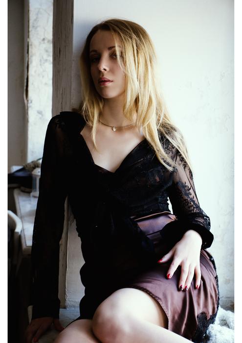 blonde in a guipure dress against a white wall