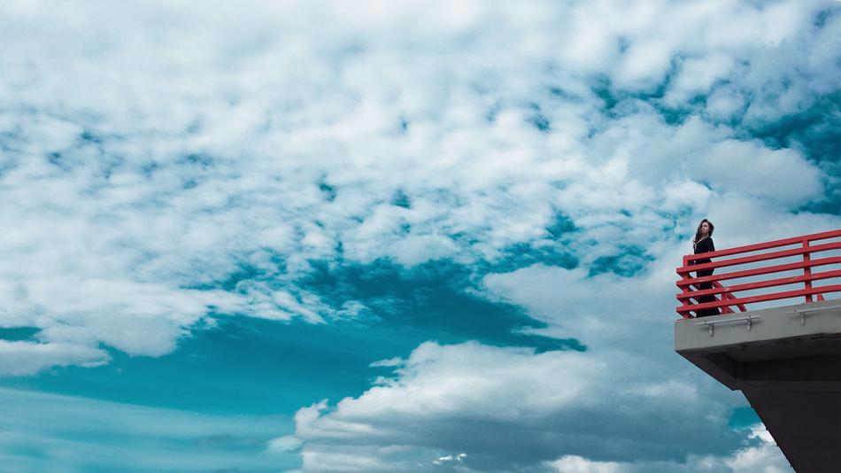 girl on the edge of the bridge against the background of white clouds