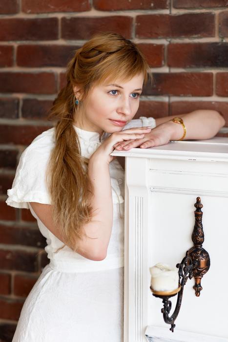 Smiling girl in white dress, posing near the beautiful white furniture with the candle