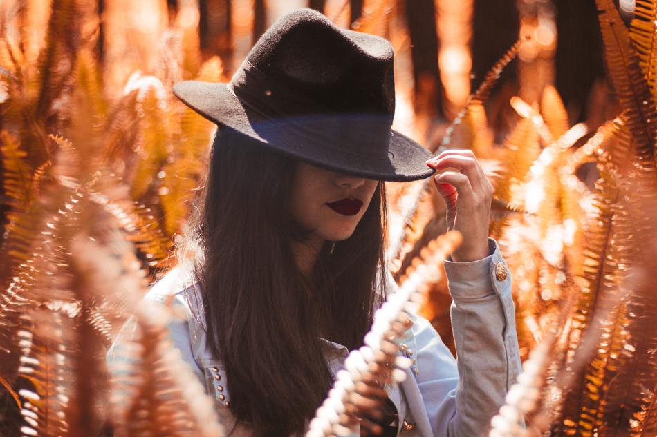 Girl covering face with hat, among the beautiful and colorful plants on the field, in sunlight
