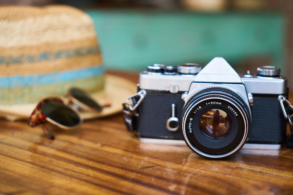 Close-up of the retro camera, sunglasses and colorful hat on the shiny, wooden table