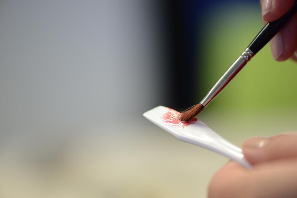 Person holding brush in the orange lip gloss, at blurred background