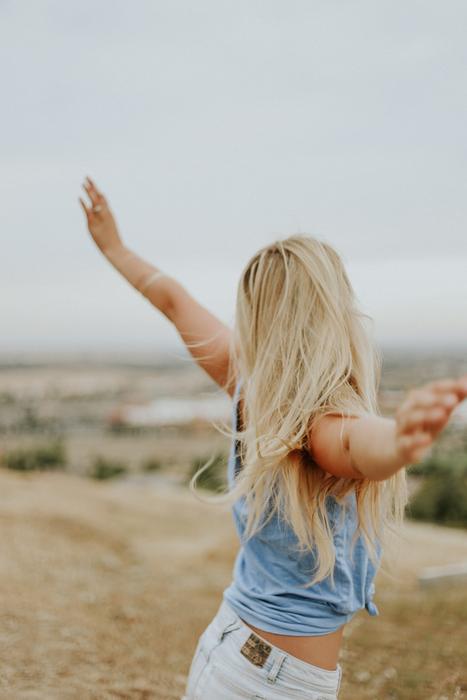 blonde woman with wide sweep of arms in a field in a blurred background