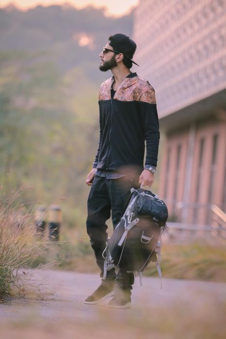 Bearded man in cap, with the backpack, near the building, among the colorful plants