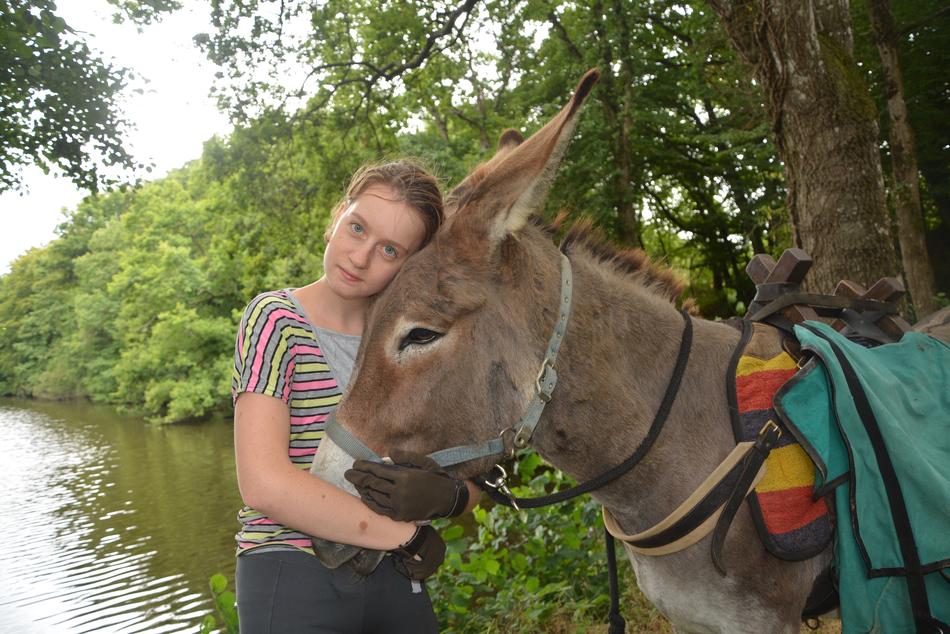 Young woman with the cute and beautiful donkey on promenade near the water, among the plants, in France