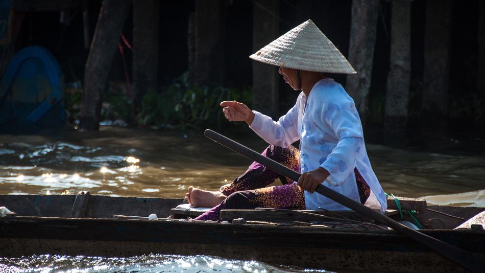Profile portrait of the woman in hat, on the boat, among the river in Vietnam