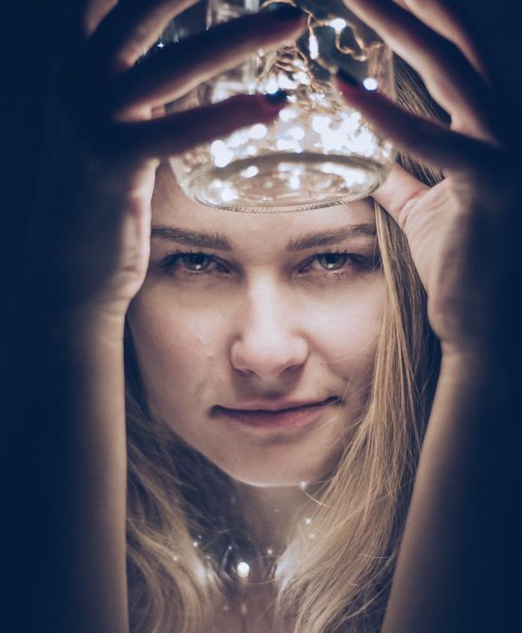 Portrait of the blonde woman, holding bottle with lights in hands, among the darkness