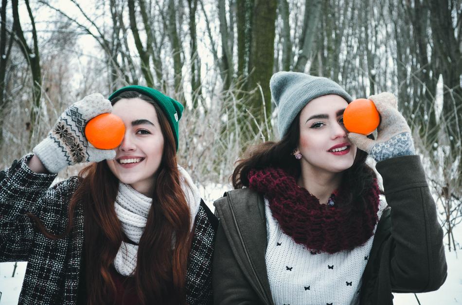 Girls in winter clothing, holding oranges among the forest in snow