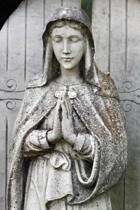 statue of the madonna on the background of doors in the cemetery